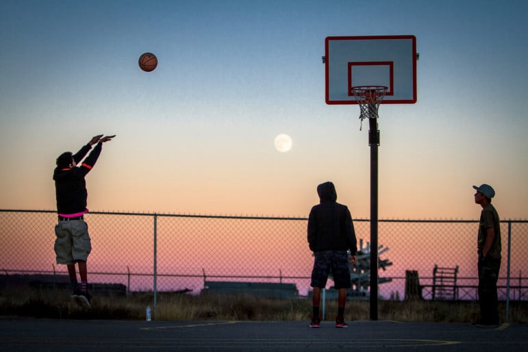 The moon rises over Thoreau as Hector Largo, left, takes a jump shot, while, Jacob James, center, and Damarco Pierce, right, await the rebound at the Thoreau Community Center basketball court in November 2014. The boys hung out at the center after school, working on homework and shooting hoops before a youth board meeting that evening. 